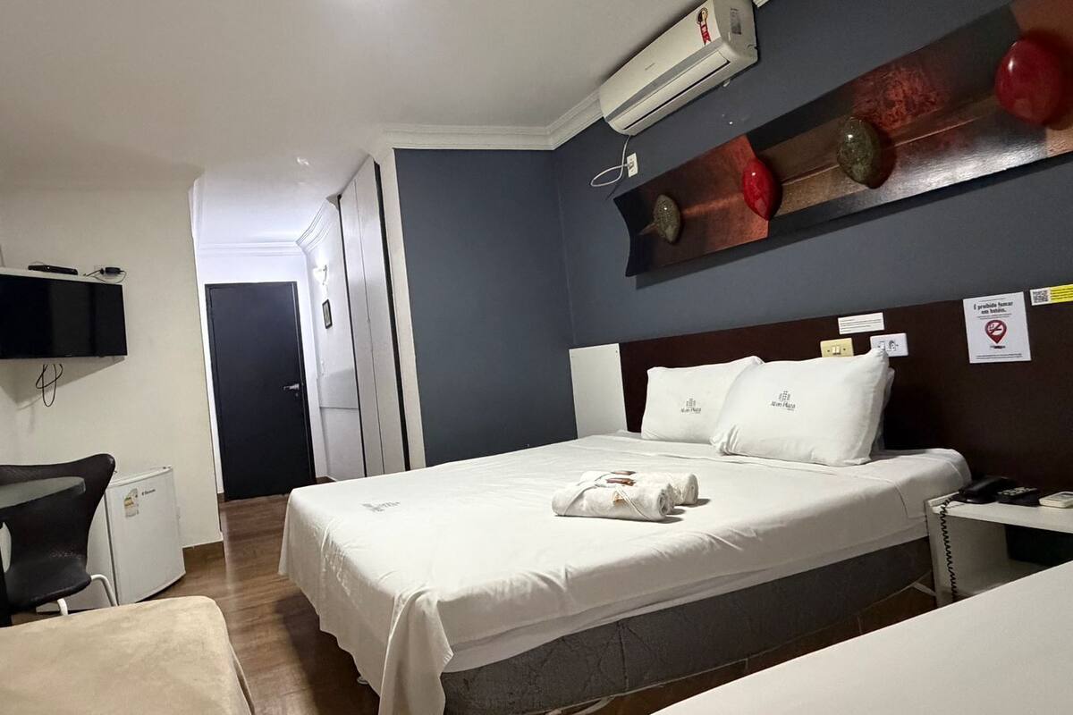 Ett hotellrum med en säng, ett skrivbord, en stol, en TV och en luftkonditioneringsanläggning.