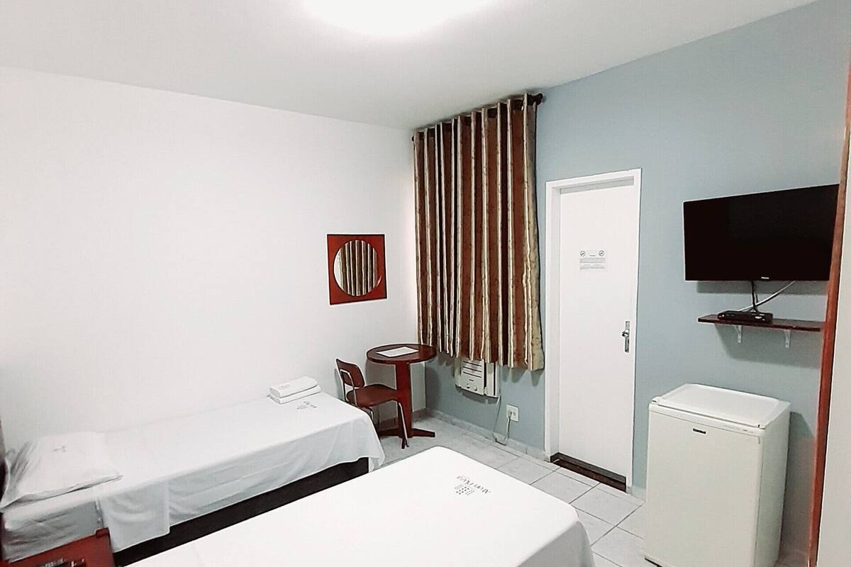 Ett hotellrum med två sängar, en tv, ett litet bord och ett kylskåp.