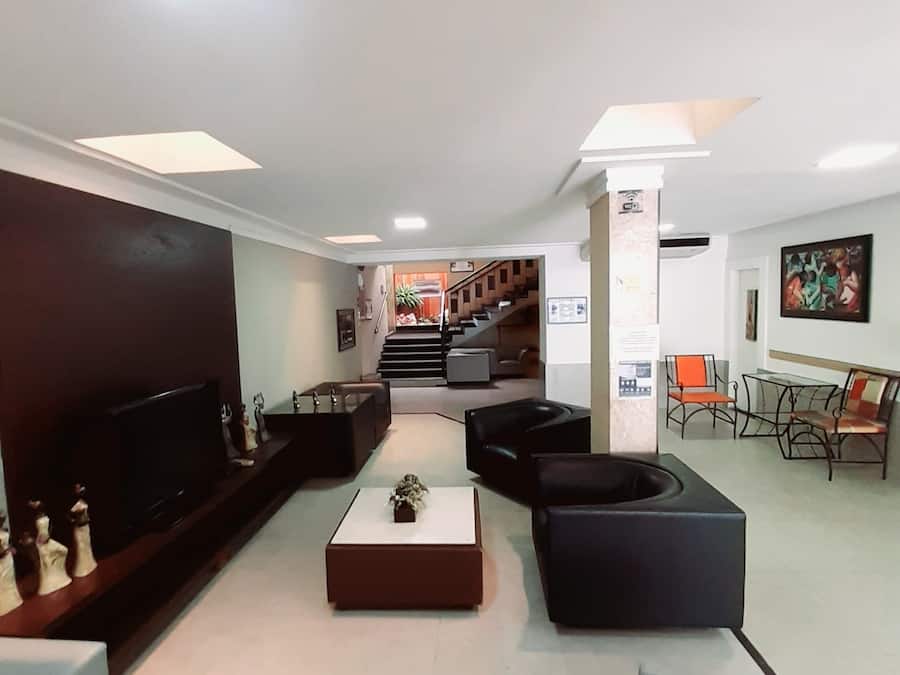 A modern lobby with a flat-screen TV, black sofas, a coffee table, and a staircase leading to an upper floor.
