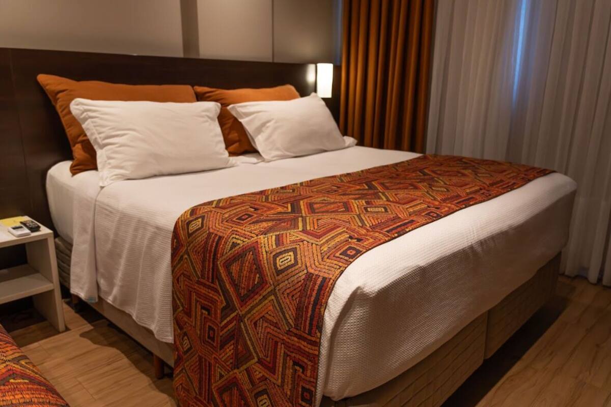 Een hotelkamer met een groot bed, wit beddengoed en een deken met een patroon.