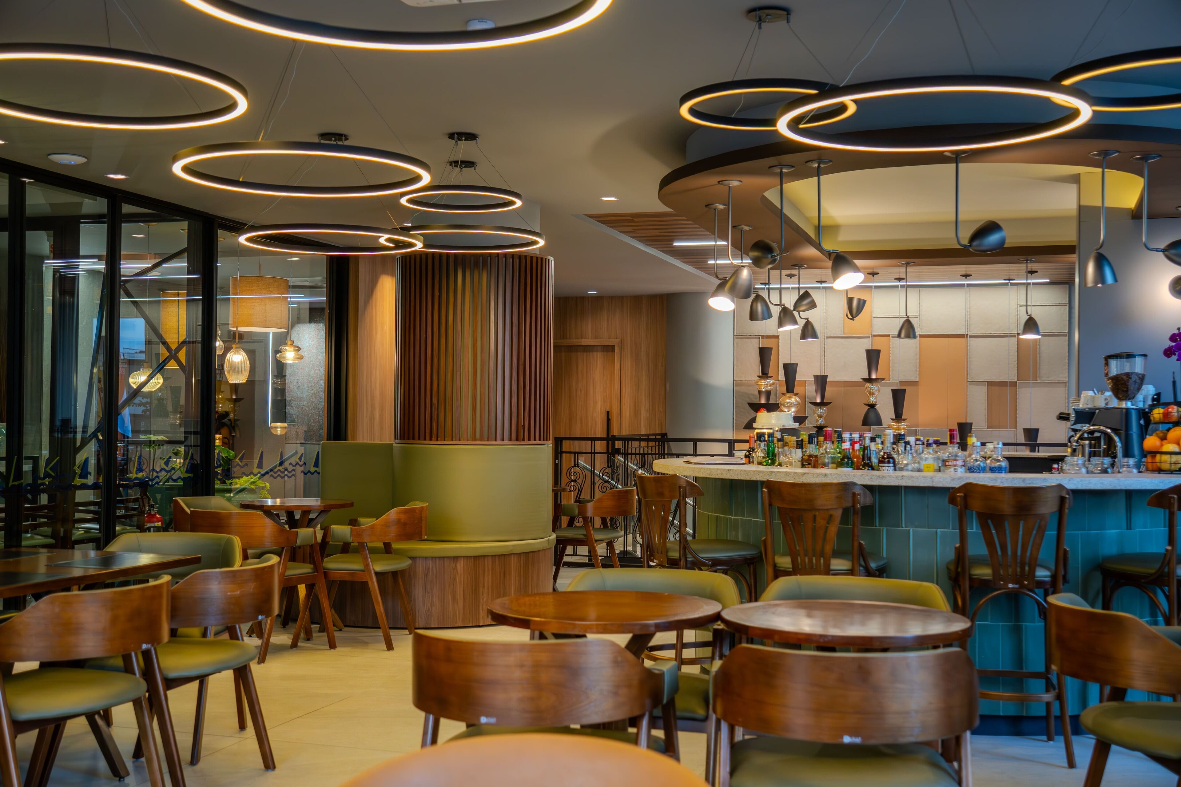 A modern restaurant interior with round tables, wooden chairs, and a bar area.