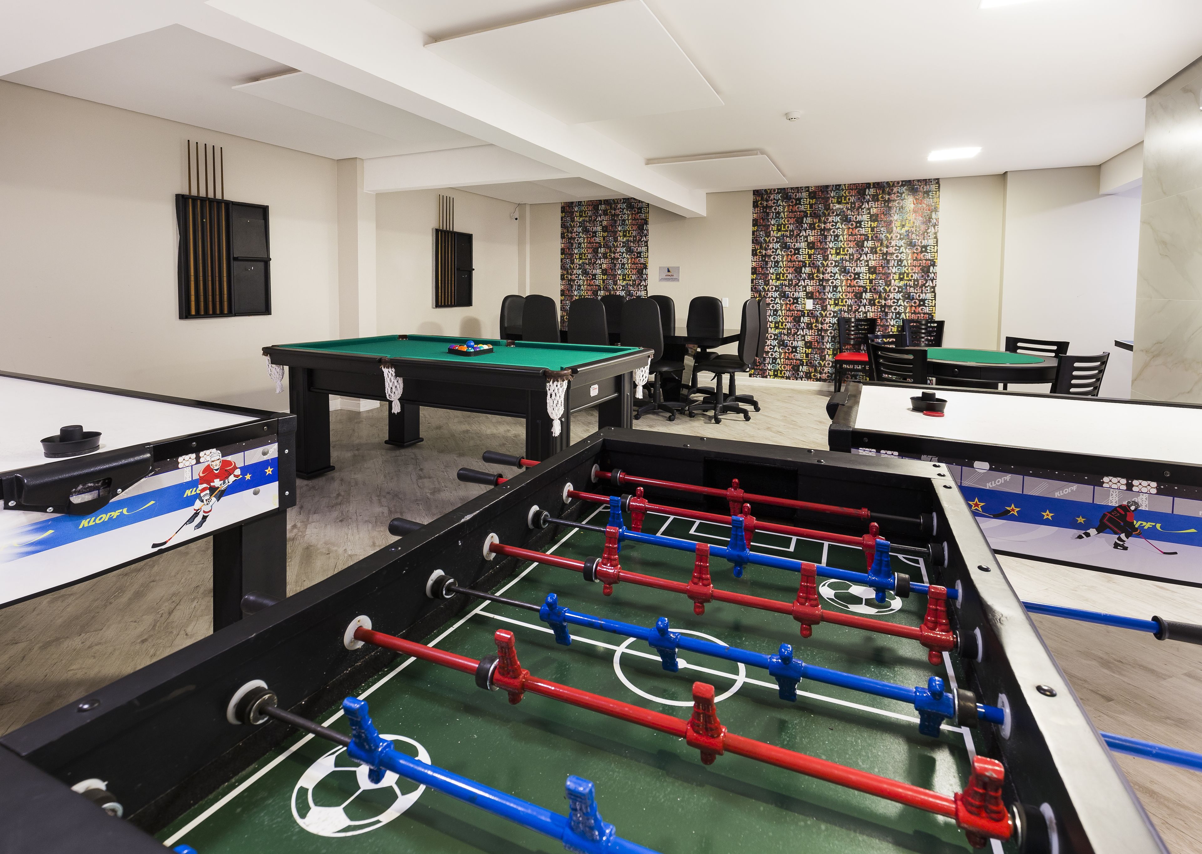 A room with multiple foosball tables, a pool table, and a seating area with chairs and a table.