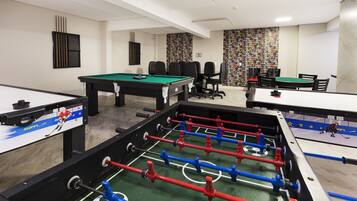A room with multiple foosball tables, a pool table, and a seating area with chairs and a table.
