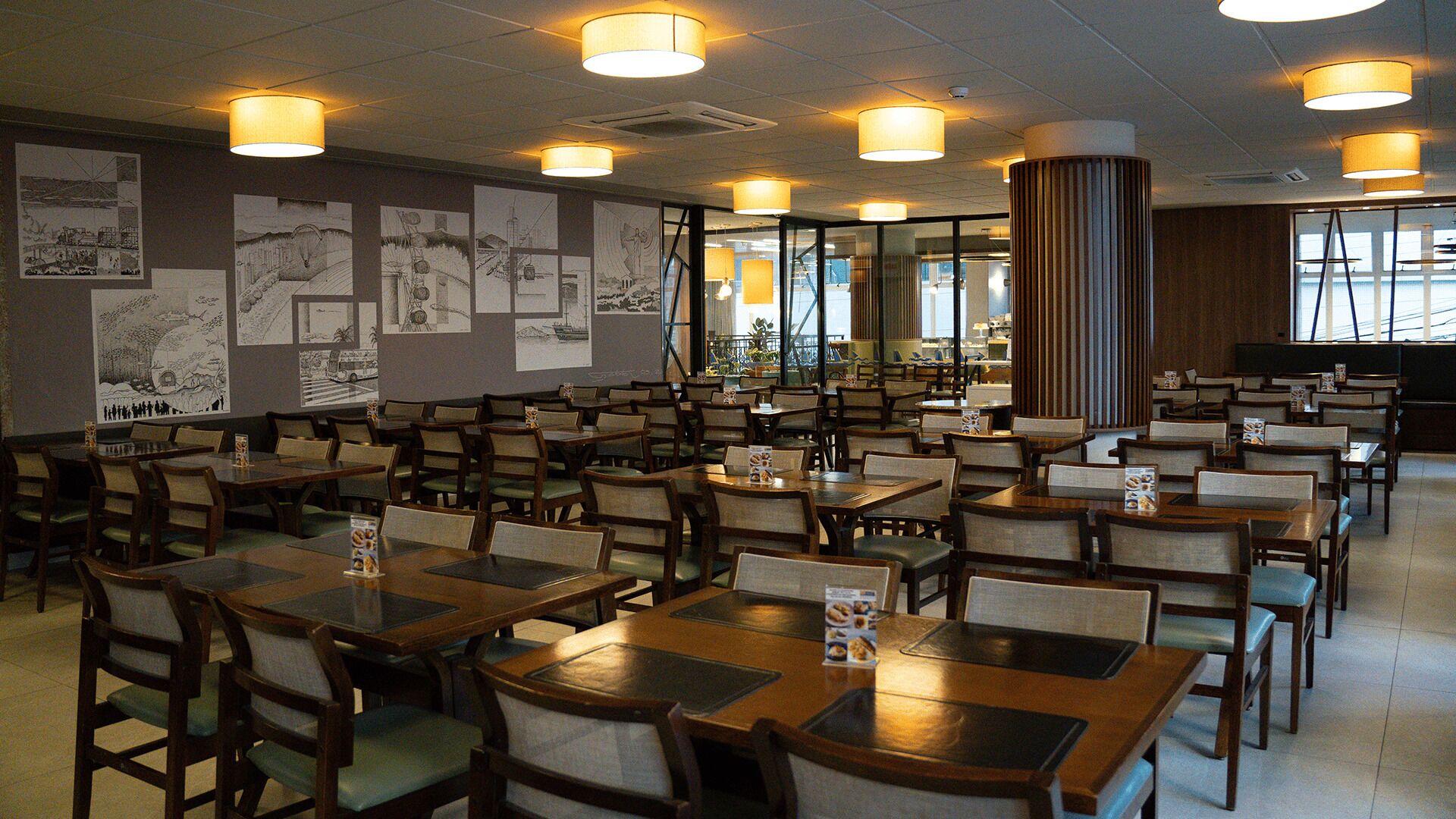 Um restaurante espaçoso com várias mesas e cadeiras, amplas janelas e obras de arte nas paredes.