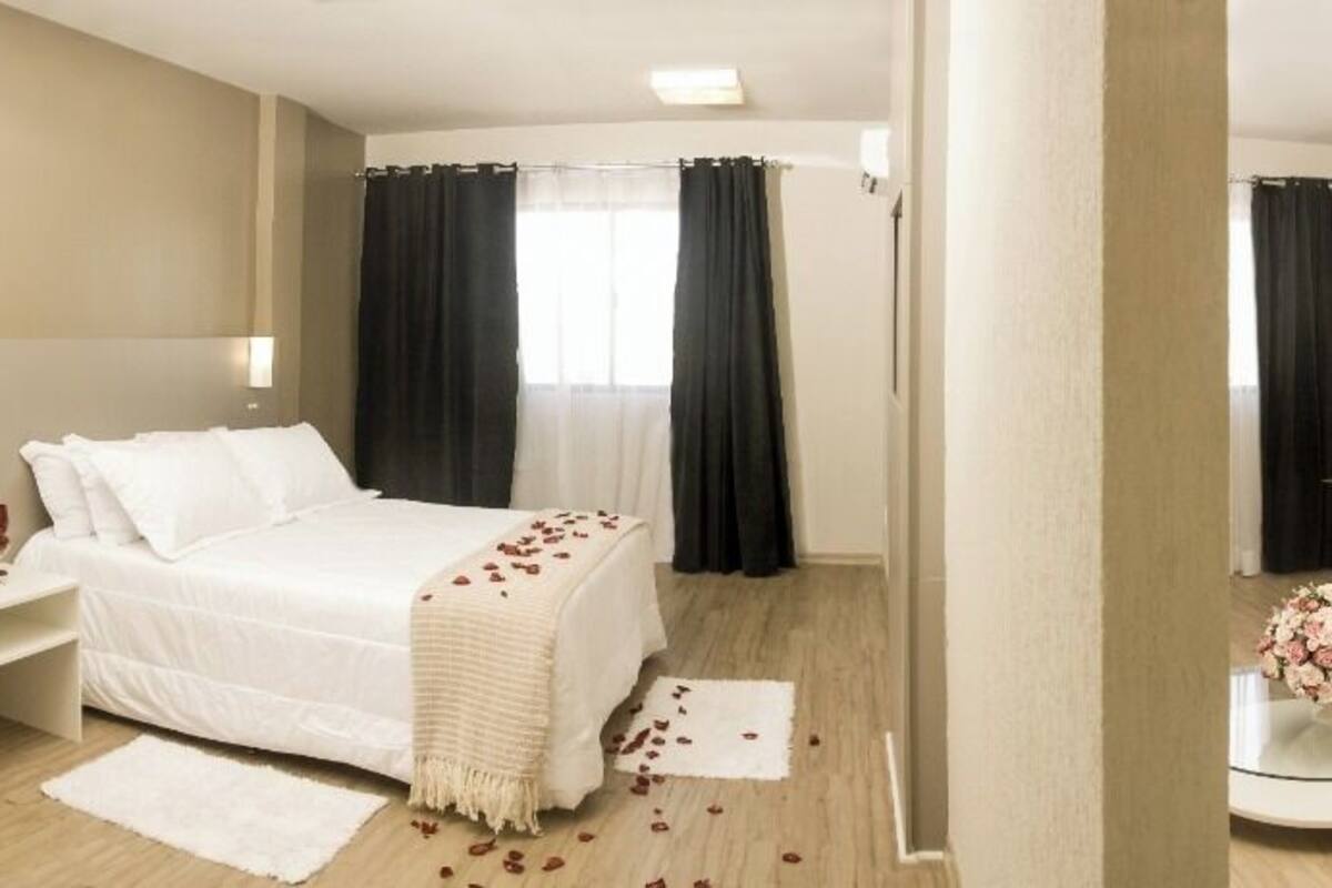 Een hotelkamer met een bed, een slaapbank, een eettafel en een bijzettafeltje met bloemen.