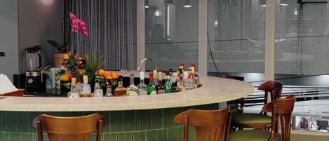 A modern kitchen with a curved island, bar stools, pendant lighting, and a view of the city through large windows.