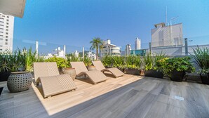 A rooftop lounge with sun loungers, potted plants, and a city skyline view. - Hotel Plaza Camboriú (Balneário Camboriú)