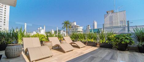 Terraza en la azotea con sillones de sol, plantas en macetas y vistas al horizonte de la ciudad.