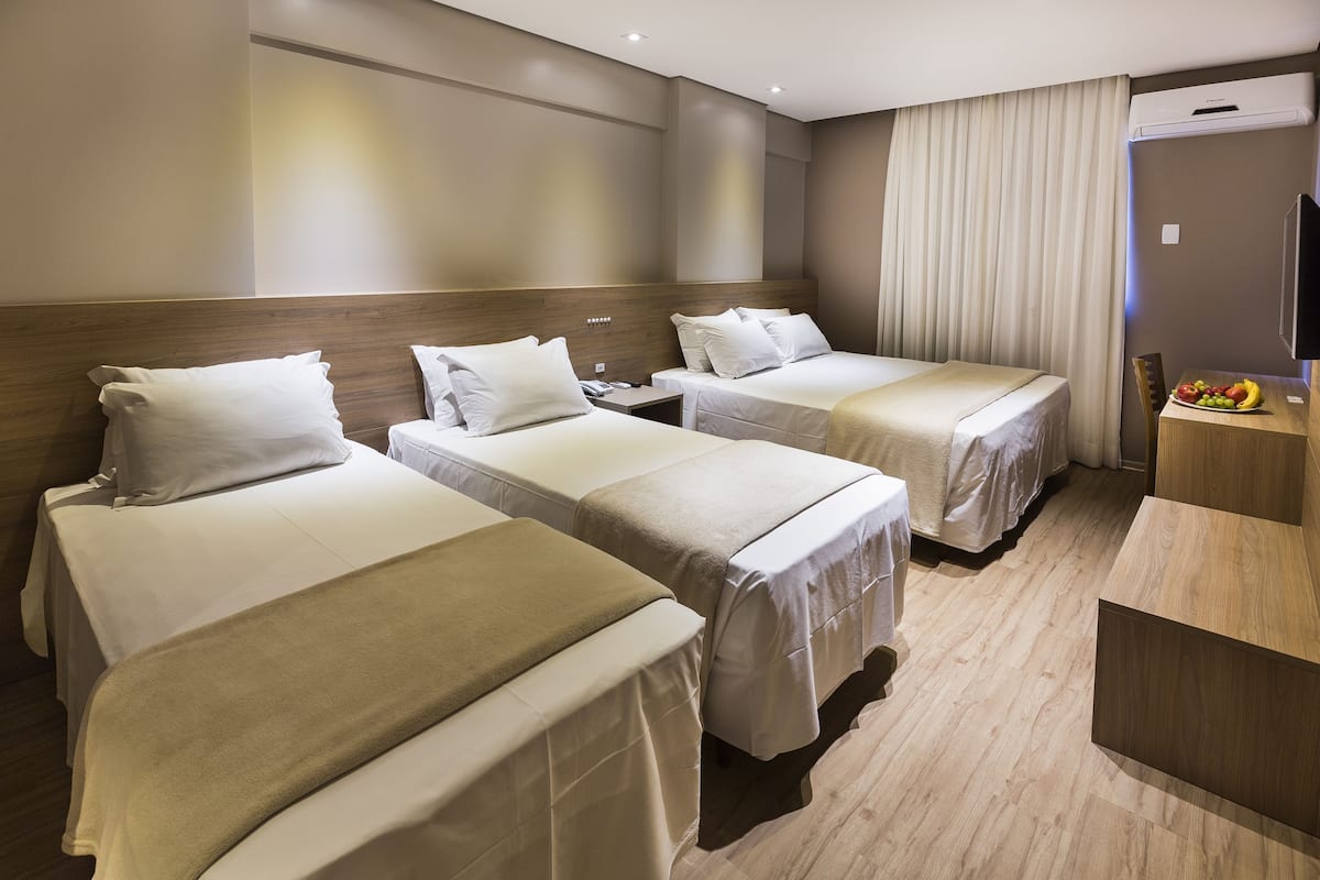 Ett hotellrum med tre sängar, en sänggavel i trä, en minibar och en fruktskål på skrivbordet.