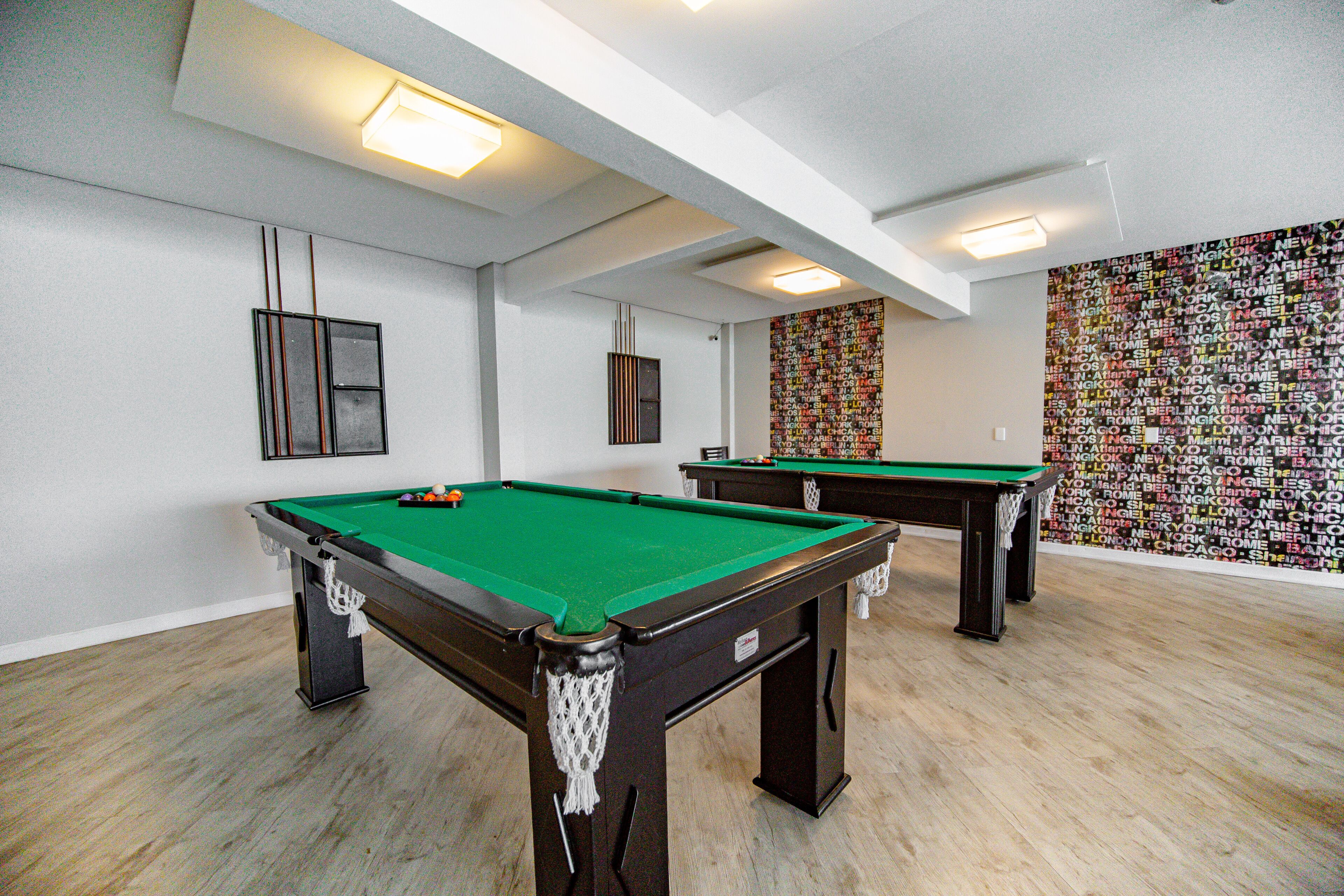 A pool room with two pool tables, a green felt surface, and a wall with city names.