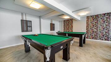 A pool room with two pool tables, a green felt surface, and a wall with city names.