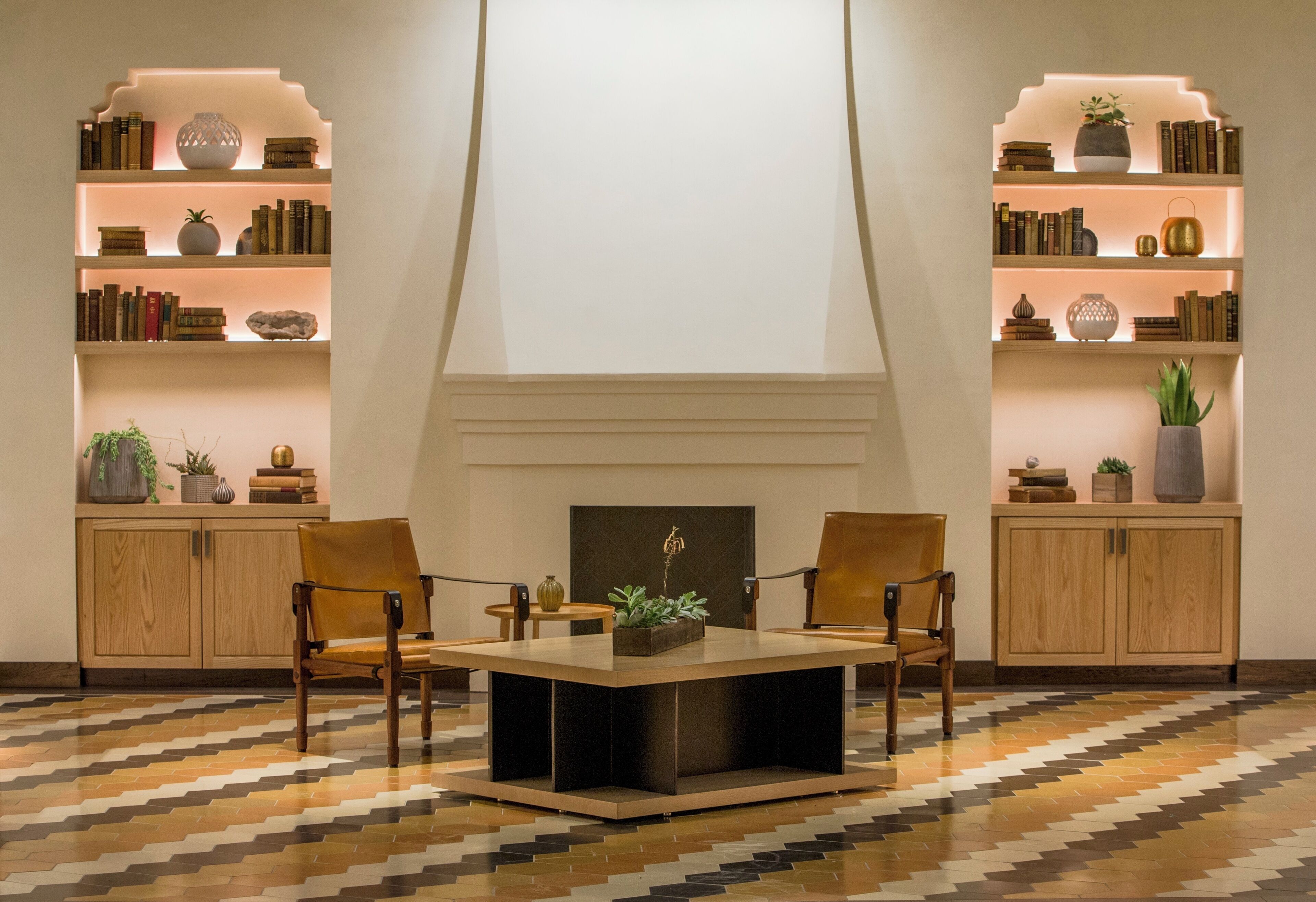 Una biblioteca moderna con estanterías, chimenea y dos sillones.