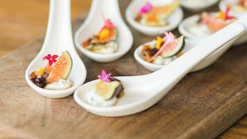 A wooden serving board with white spoons containing food garnished with flowers.
