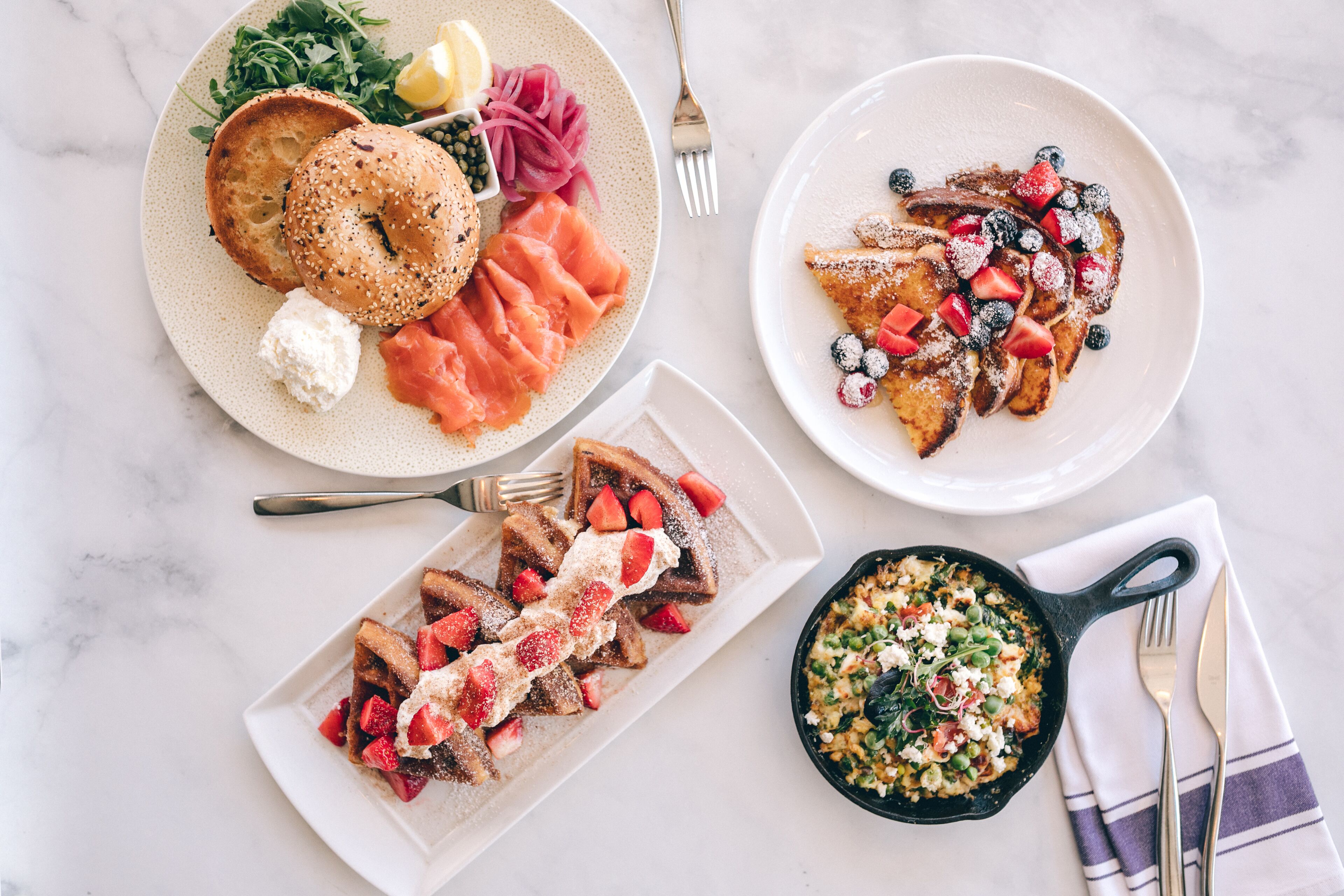 A breakfast setting with bagels, smoked salmon, pancakes with berries, and a skillet of eggs.
