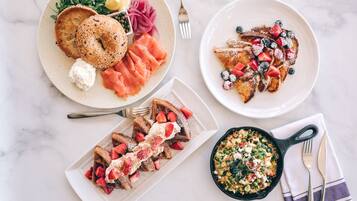 A breakfast setting with bagels, smoked salmon, pancakes with berries, and a skillet of eggs.