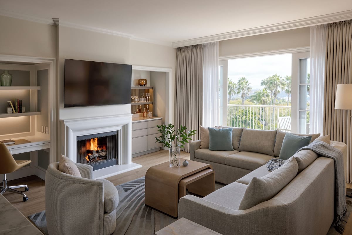 A modern living room with a fireplace, a flat-screen TV, a sofa, a coffee table, and a view of the outdoors.