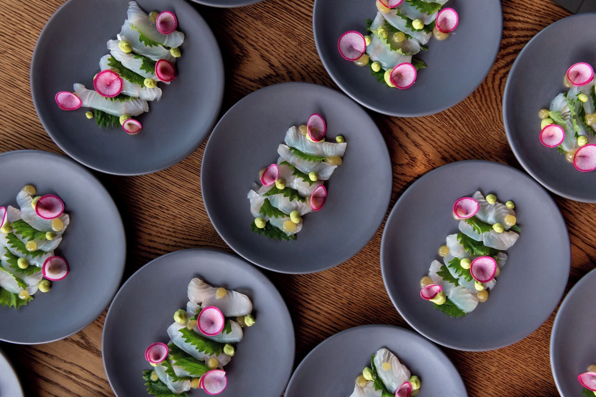 Multiple gray plates with a seafood dish, arranged on a wooden surface.
