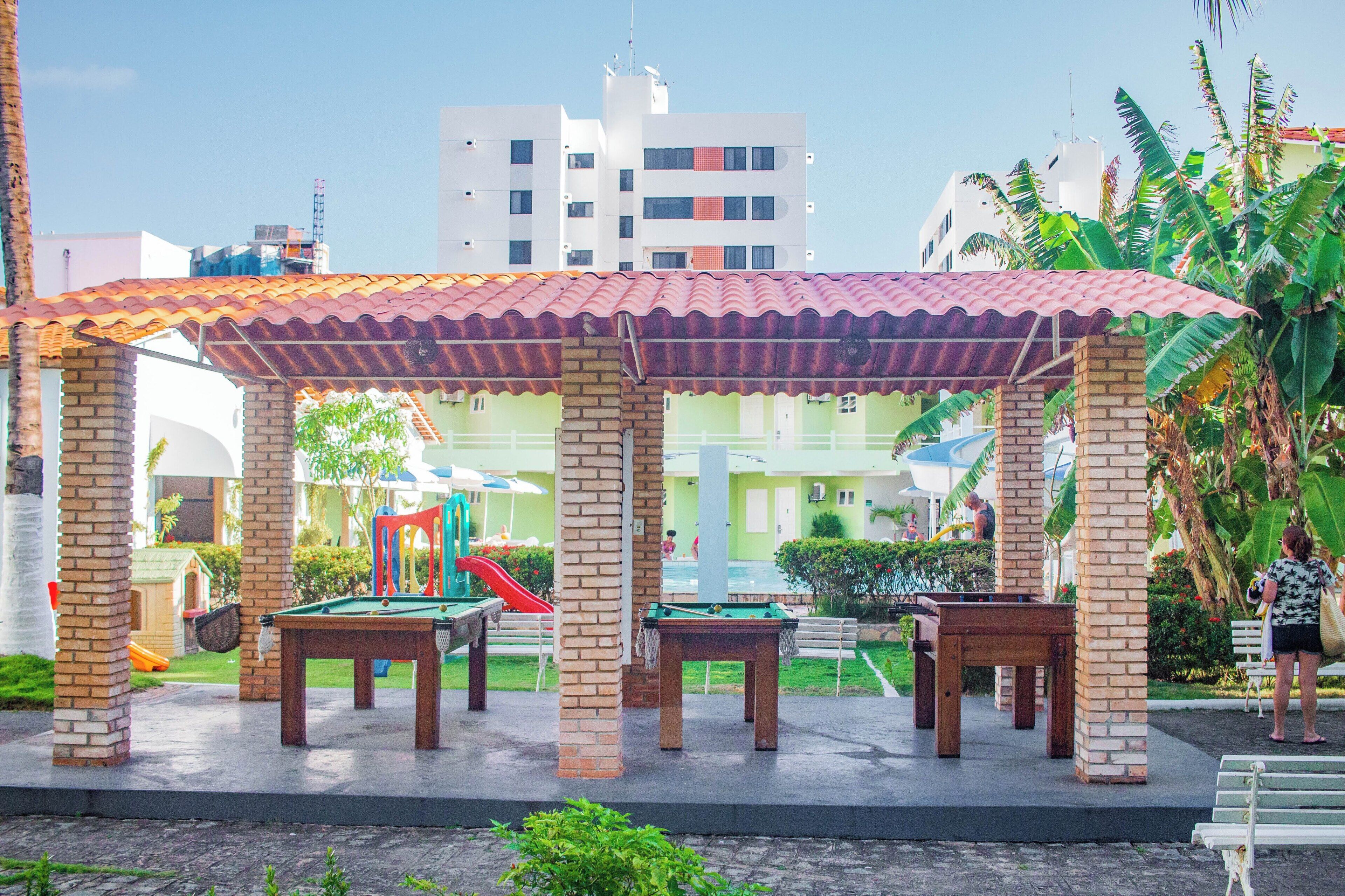 Un espacio al aire libre cubierto con mesas y sillas, piscina y parque infantil.