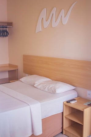 A neatly made bed with a wooden headboard, a bedside table with a remote control, and a wall-mounted light fixture. - Hotel Parque das Águas (Aracaju)
