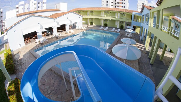 A pool area with a water slide, lounge chairs, and umbrellas. - Hotel Parque das Águas (Aracaju)