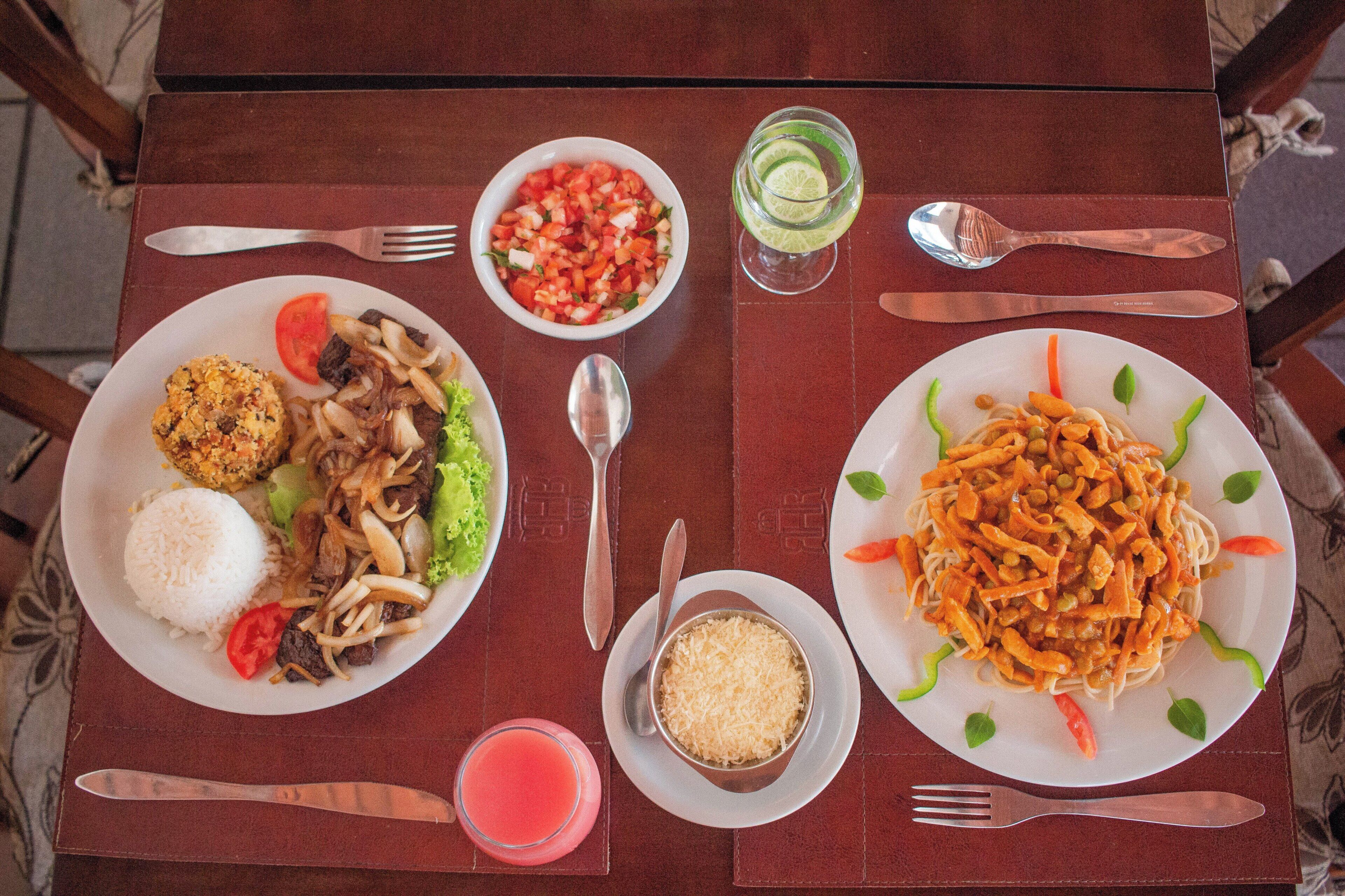 A table with plates of food, a glass of drink, and cutlery.