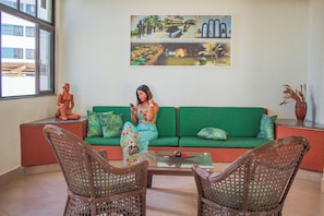 Una habitación con un sofá verde, sillas de mimbre, una mesa de centro de vidrio y un cuadro en la pared.