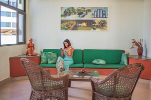 Ein Zimmer mit einem grünen Sofa, Korbstühlen, einem Glastisch und einem Bild an der Wand.