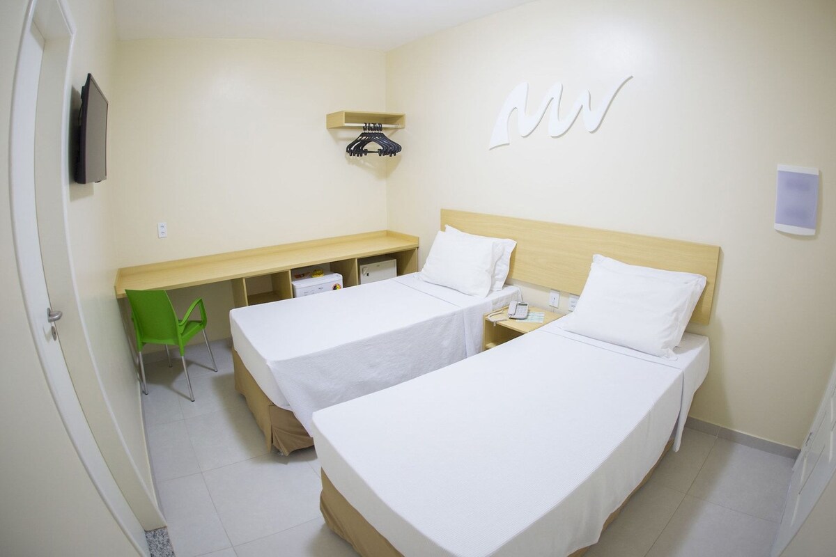 A hotel room with two beds, a desk, a chair, and a bedside table with a phone.
