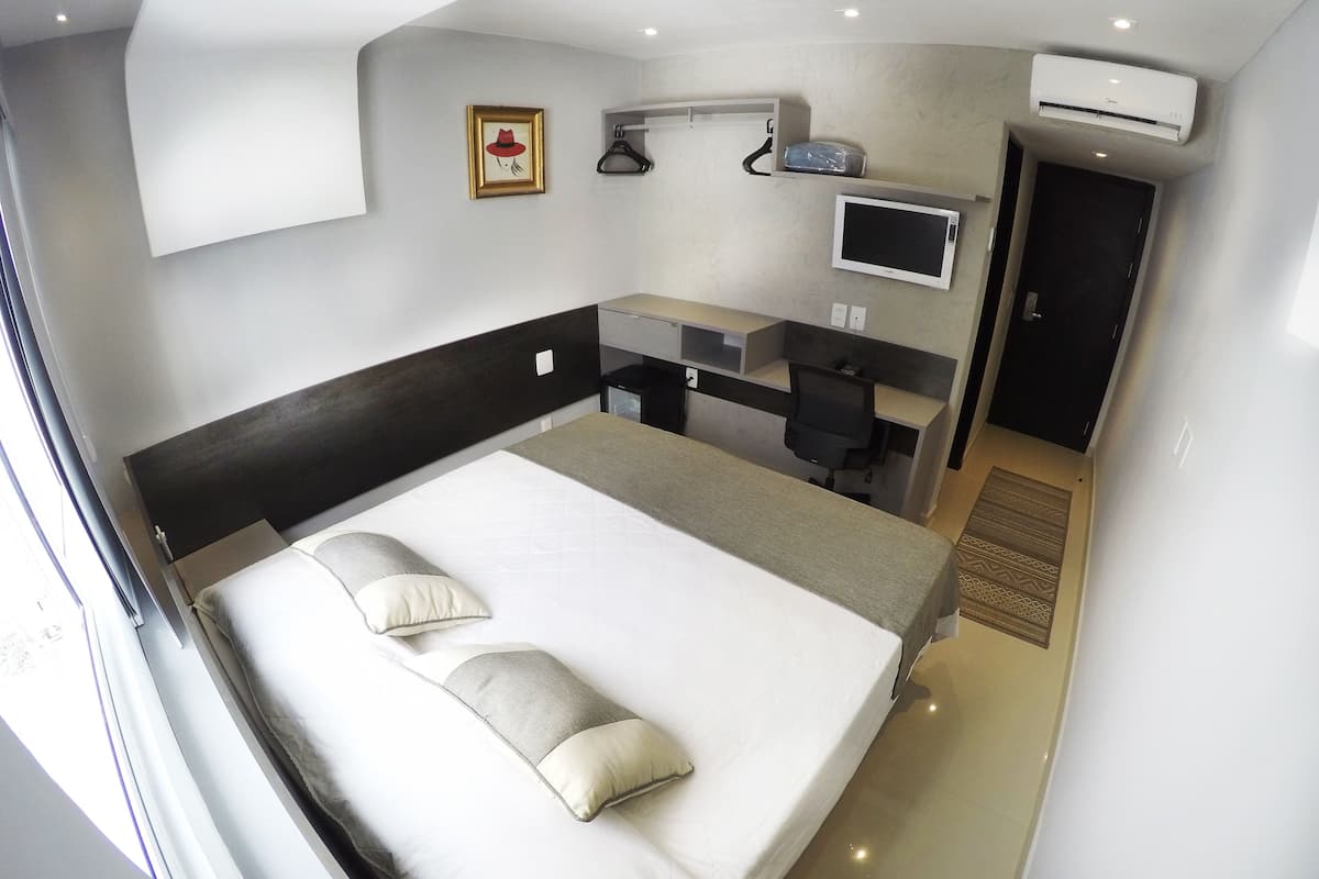A modern hotel room with a large bed, a desk, a chair, a flat-screen TV, and an air conditioning unit.