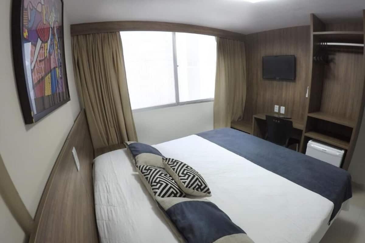 A hotel room with a large bed, a desk, a television, and a wardrobe.