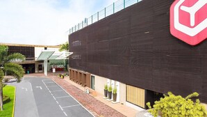 A modern building with a prominent logo, a parking area, and a pathway leading to the entrance. - Dublê Hotel (Recife)