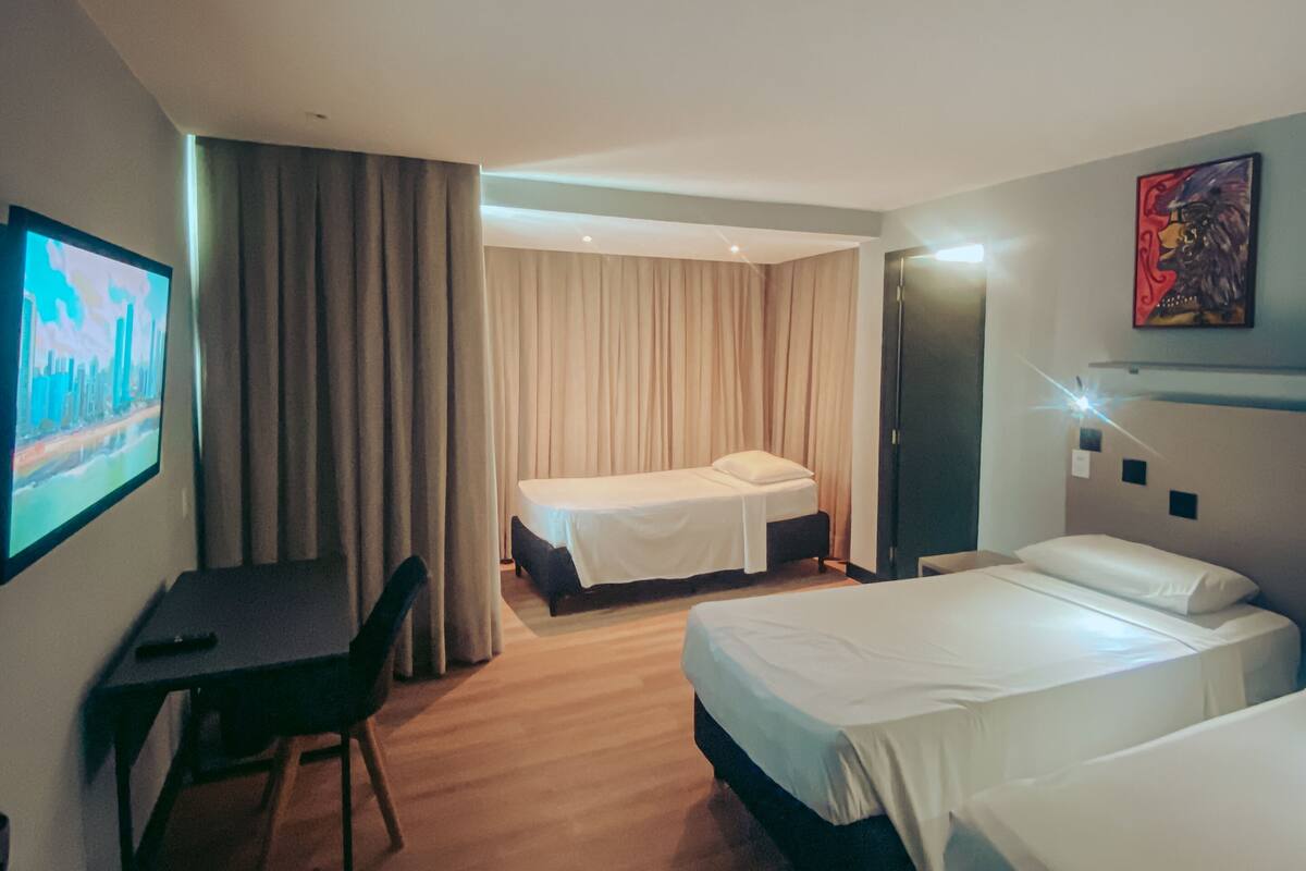 A hotel room with two beds, a desk, a chair, a TV, and a painting on the wall.
