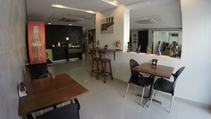 A modern cafe with wooden tables and black chairs, a Coca-Cola mural, and a coffee menu on the wall. - Dublê Hotel (Recife)