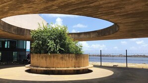 A circular outdoor area with a central planter, under a large overhang structure, overlooking a body of water. - Dublê Hotel (Recife)