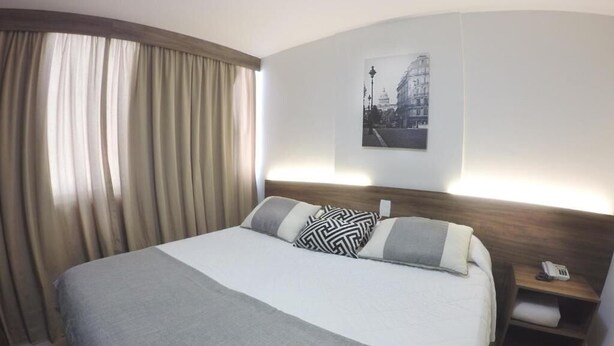 A hotel room with a large bed, a nightstand with a phone, and a wall-mounted picture. - Dublê Hotel (Recife)