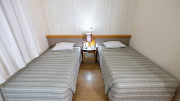 Habitación de hotel con dos camas individuales, una mesita de noche con lámpara y cabecero de madera.