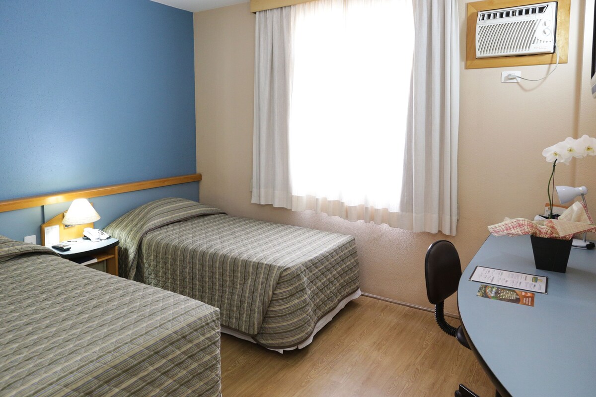 Habitación de hotel con dos camas, un escritorio con teléfono, una silla y una ventana con cortinas.