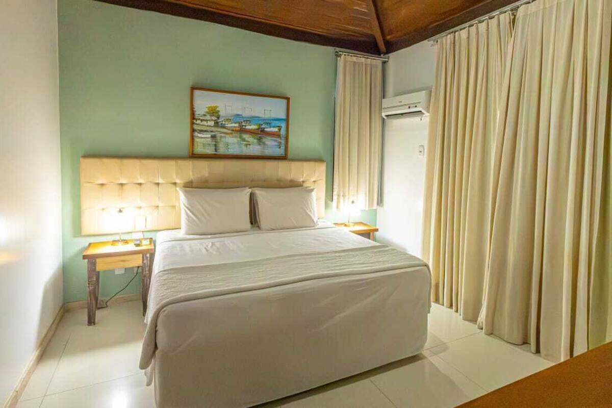 A bedroom with a bed, a nightstand, a painting on the wall, and curtains.
