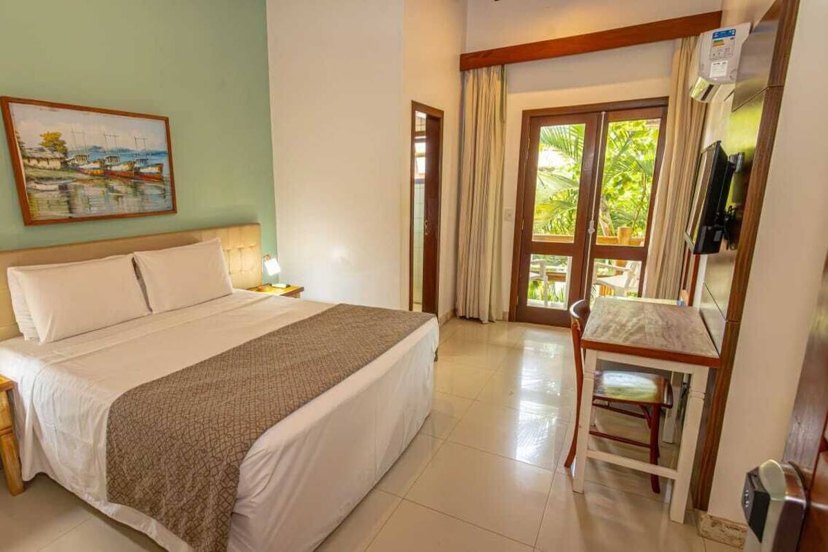 A hotel room with a bed, bedside table, lamp, and a painting on the wall.