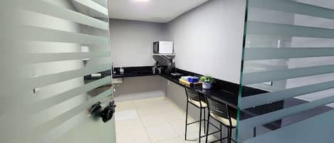 A kitchen with a microwave, a sink, and a bar stool.