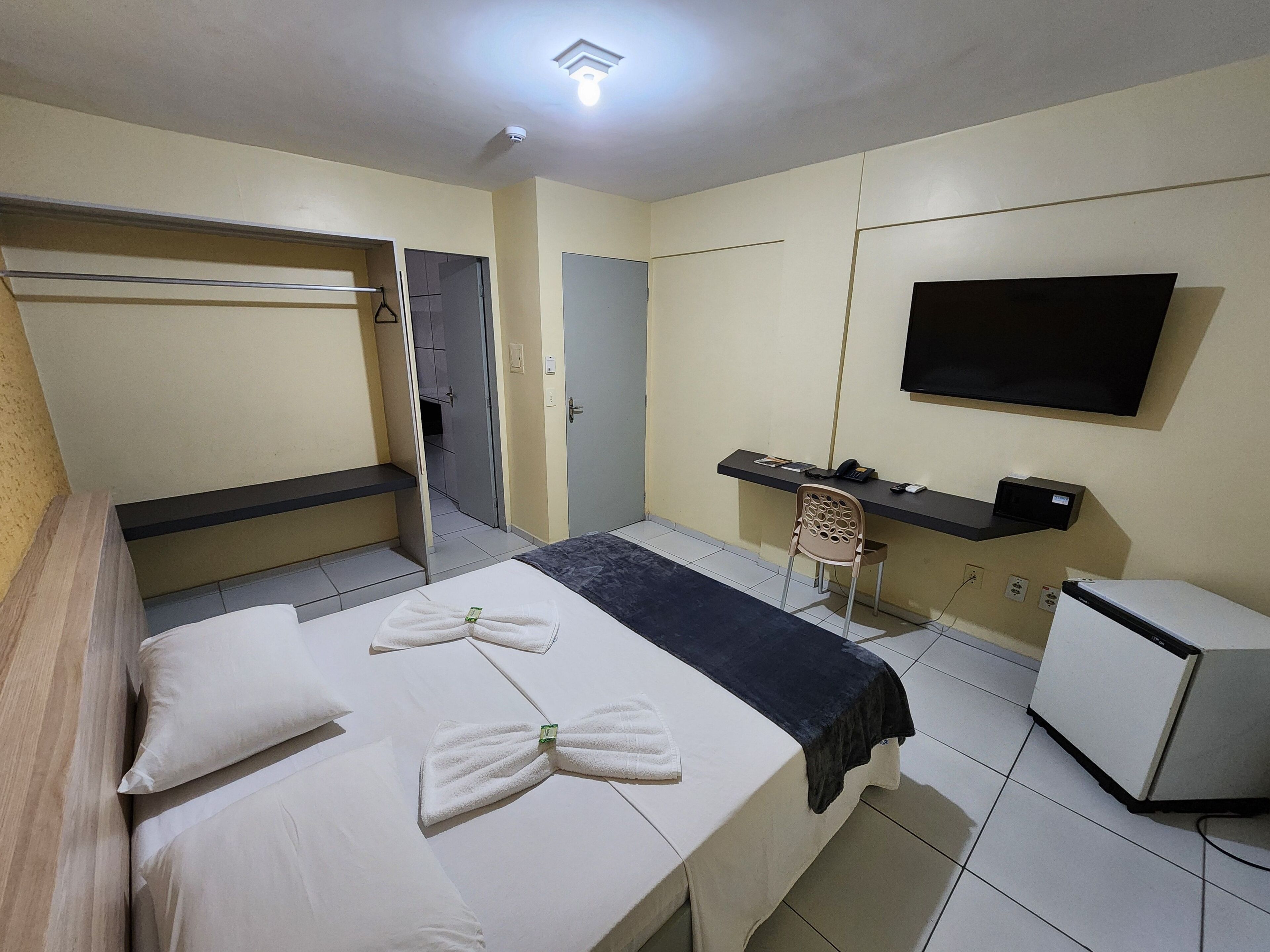 A hotel room with a bed, a desk, a TV, and a refrigerator.