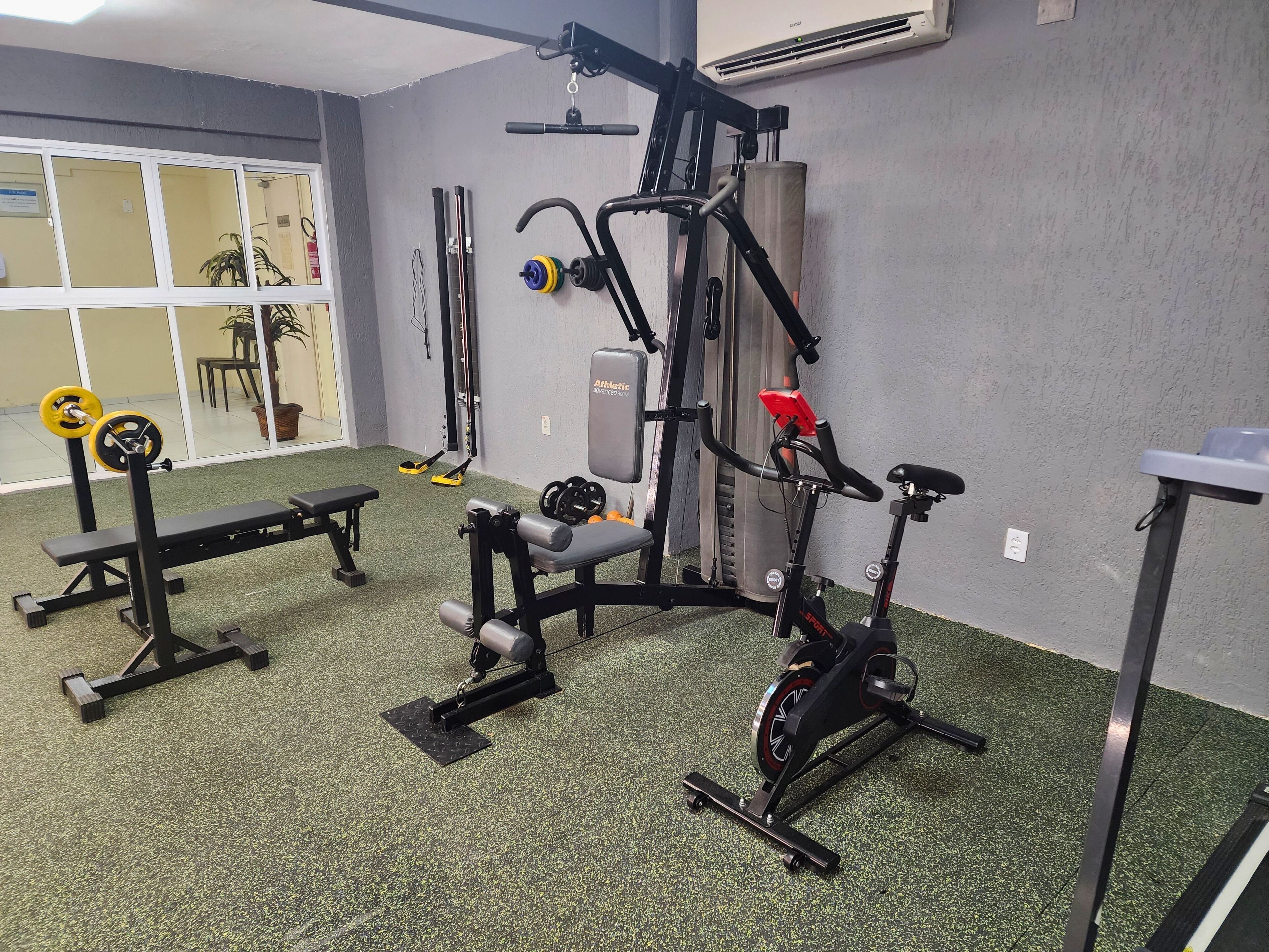 Ein Fitnessraum mit Trainingsgeräten, einer Bank und einem Ergometer.
