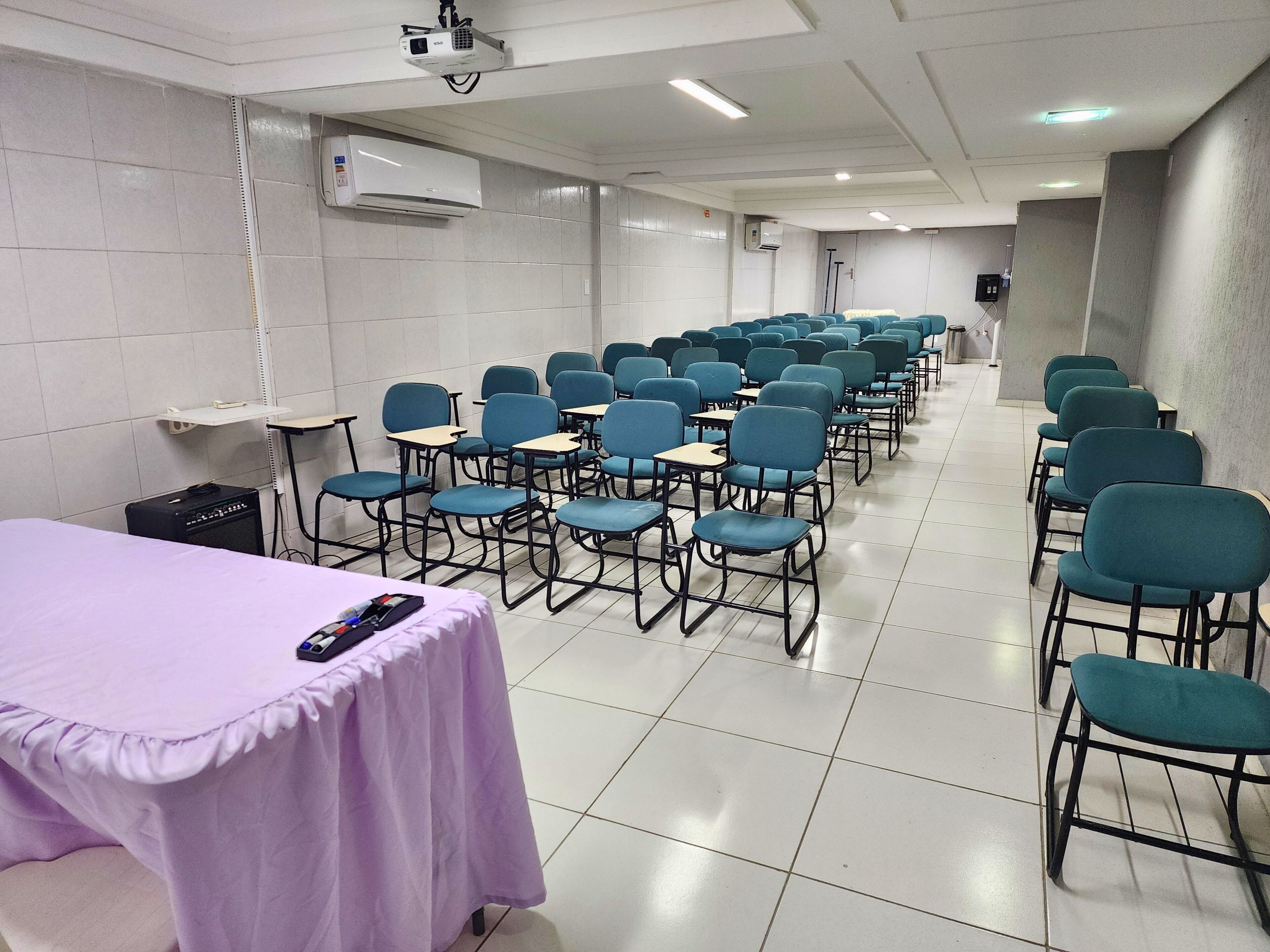 A conference room with rows of chairs, tables, a projector, and an air conditioning unit.