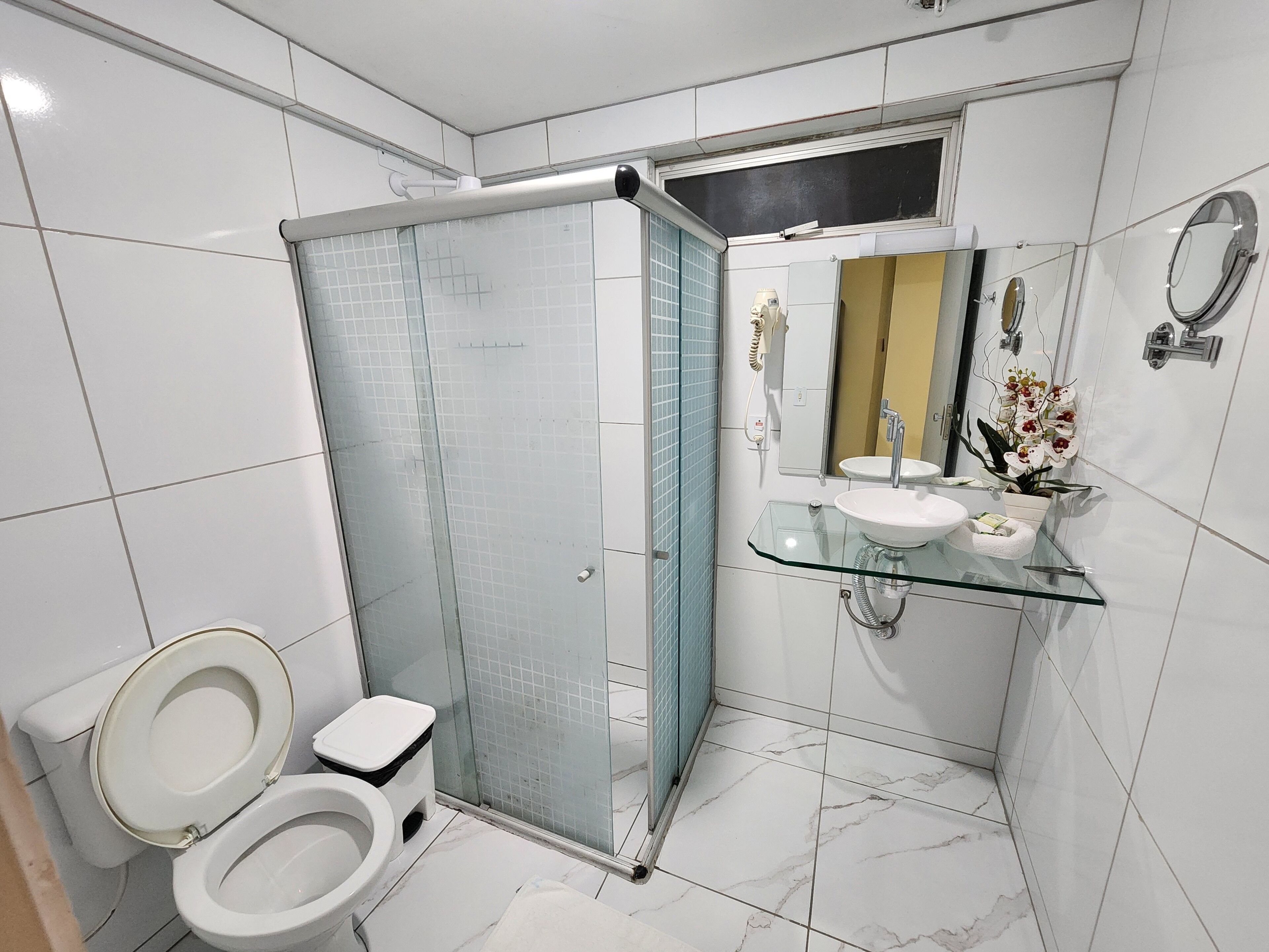 A modern bathroom with a glass shower enclosure, a toilet, and a glass vanity with a sink and mirror.