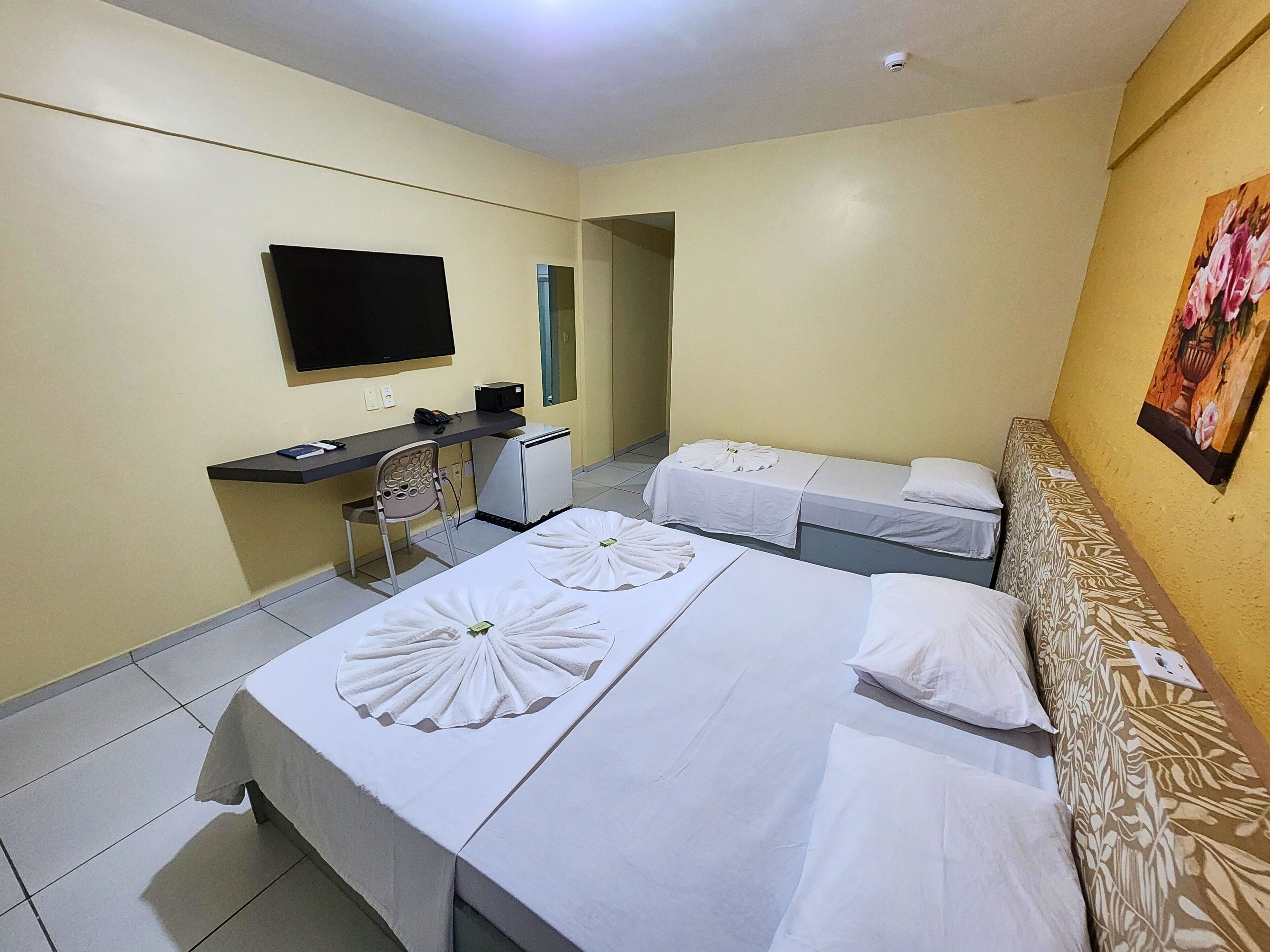 A hotel room with two beds, a desk with a computer, a TV, and a small refrigerator.