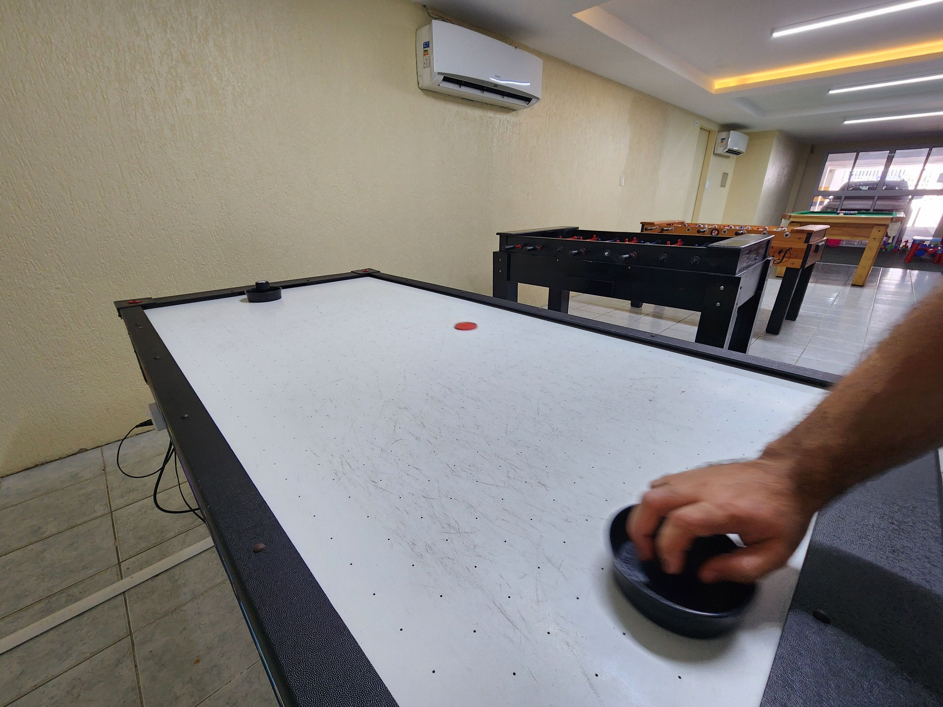 A foosball table in a room with a tiled floor, a wall-mounted air conditioner, and a window with blinds.