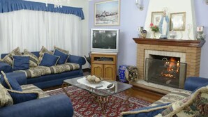 A living room with a blue sofa set, a fireplace, a television, and a chandelier. - Shallon (Campos do Jordão)