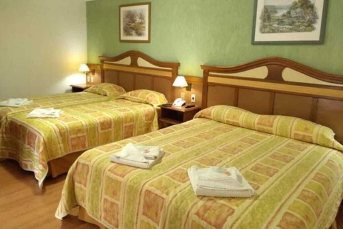 Una habitación de hotel con dos camas, cada una con cabecero de madera, una mesita de noche con lámpara y un cuadro enmarcado en la pared.