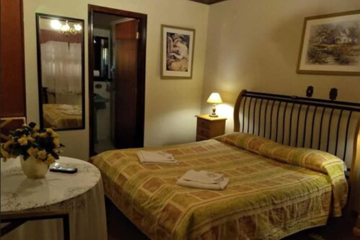 A hotel room with a bed, a bedside table with a lamp, a mirror, and a painting on the wall.