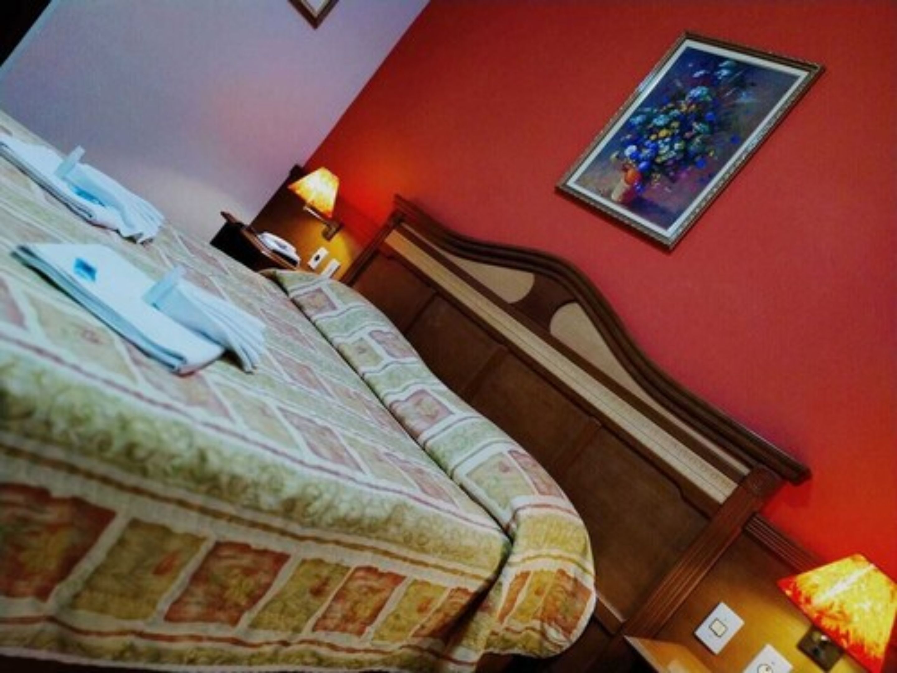 A hotel room with a bed, a nightstand, a lamp, and a painting on the wall.